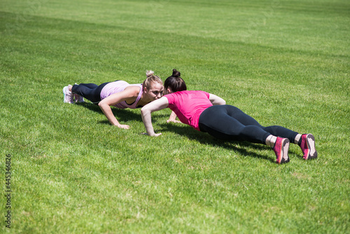 Two women doing push-ups on the grass in the stadium. Practicing gym