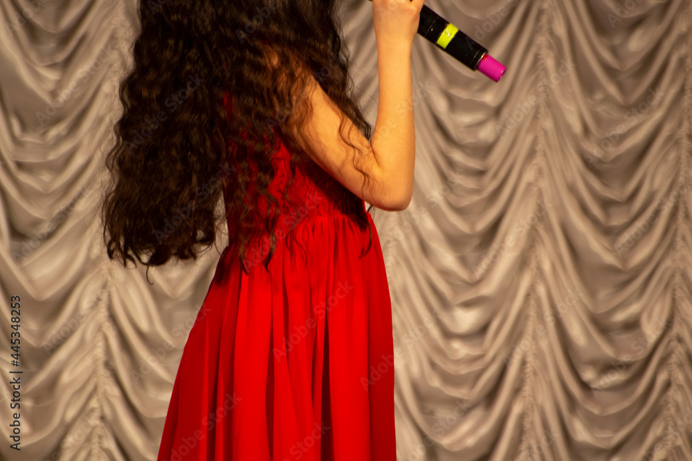 Fototapeta premium The girl sings into the microphone. A child in a red dress on stage.