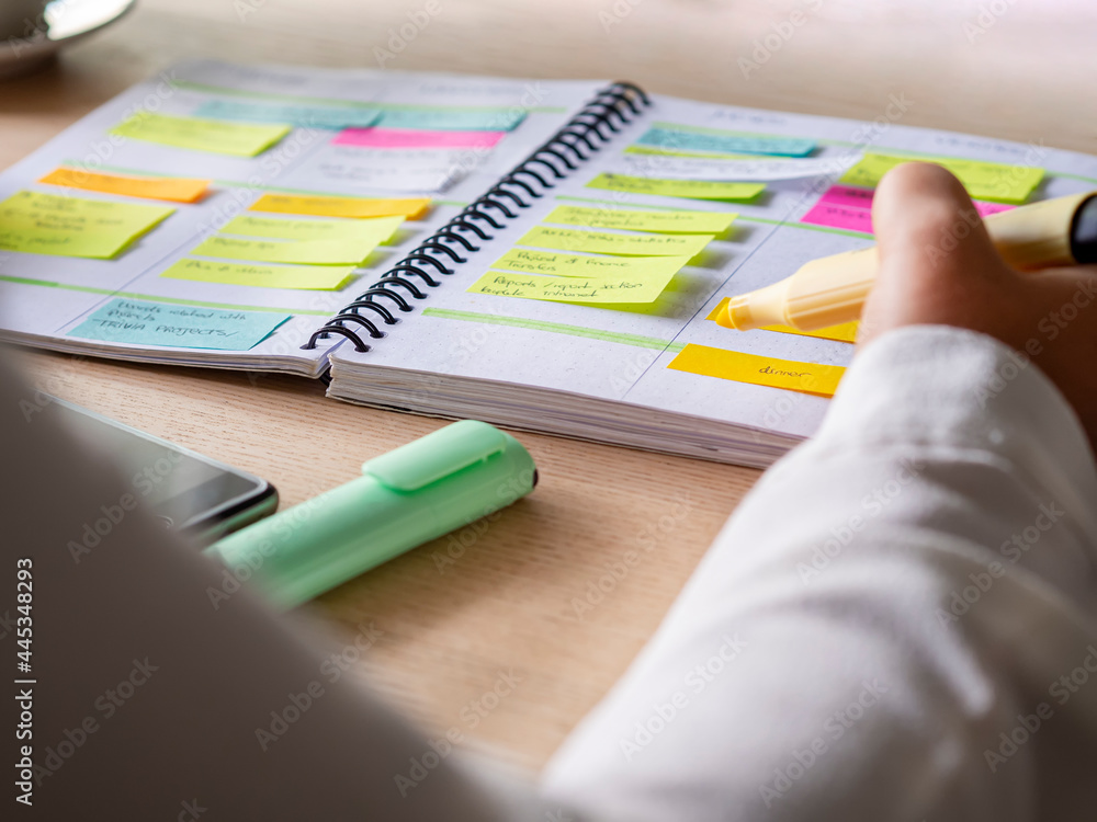 Close-up of agenda organize with color-coding sticky notes for time management. Productive schedule for appointments and reminders. Hand holding a yellow highlighter marker. Organization and planning - obrazy, fototapety, plakaty 