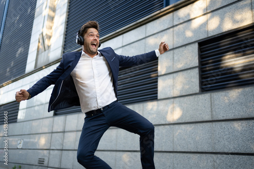 Fotografia Business man wearing headphones in a blue suit, jumping in the street