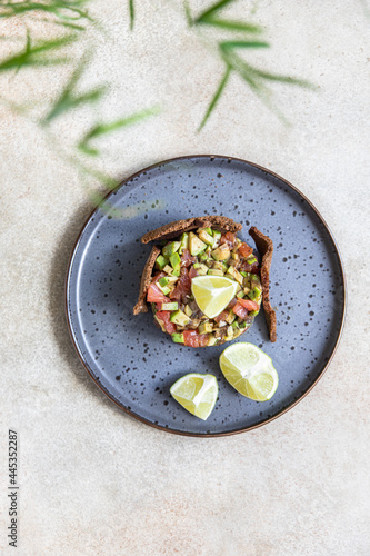 Raw tuna and avocado tartar served with rye bread crackers and lime on black ceramic plate. Gourmet fish tartar. photo