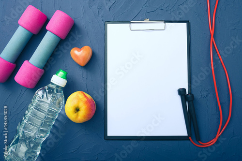 sports equipment - dumbbells, an apple and a bottle of water and a jump rope, a blank sheet of paper to record achievements
