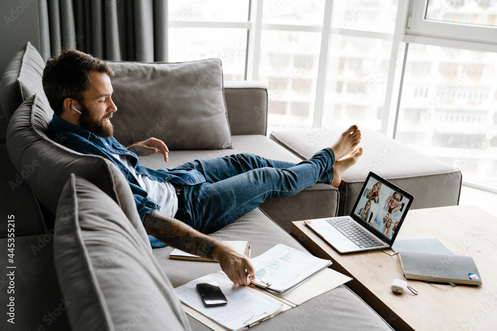 Bearded man making conference call on laptop while sitting on sofa Bearded man making conference call on laptop while sitting on sofa