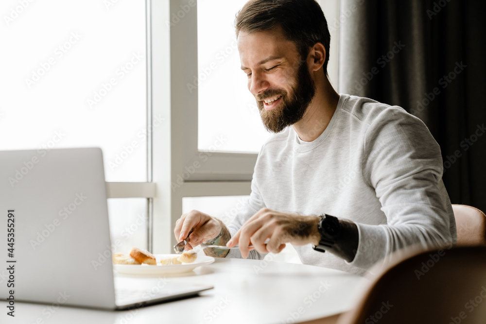 Bearded european man working with laptop while having breakfast Bearded european man working with laptop while having breakfast