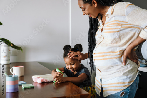 Black woman and her daughter smiling Black pregnant woman smiling while stroking her daughter's head writing in exercise books photo