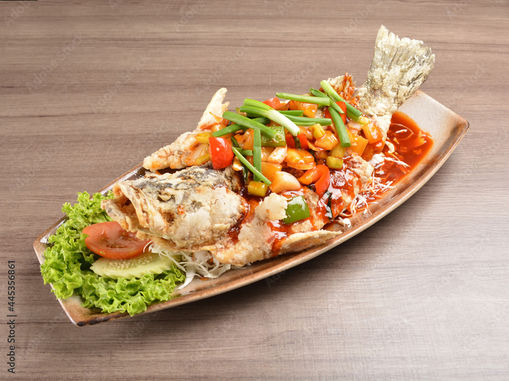 deep fried crispy whole grouper fish with vegetables in sweet and sour sauce on wood background asian halal menu