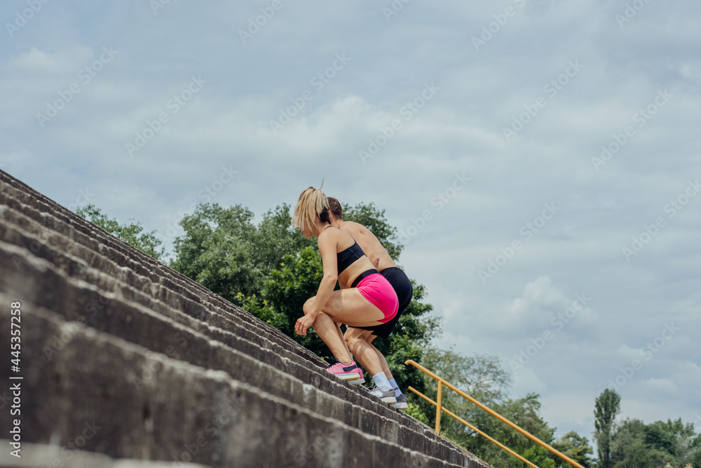 Naklejka premium Below view of young male and female athletes jumping upstairs on the outdoor staircase .