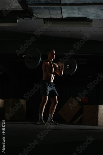  Silhouette of a fit strong shirtless athlete doing squats. Weight lifting workout concept.