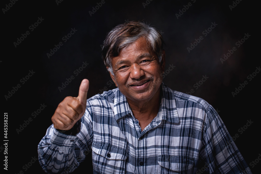 Smiling happy elderly man sitting and thumbs up looking at camera on black background, in studio Smiling happy elderly man sitting and thumbs up looking at camera on black background, in studio