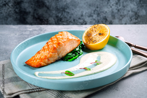 Grilled salmon steak with spinach, lemon and sauce on a plate. Salmon fillet dish served in the restaurant