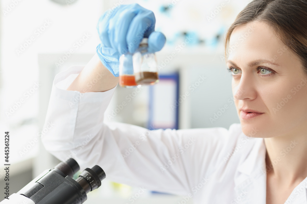 Woman scientist chemist holding glass jars with medicine in front of microscope Woman scientist chemist holding glass jars with medicine in front of microscope