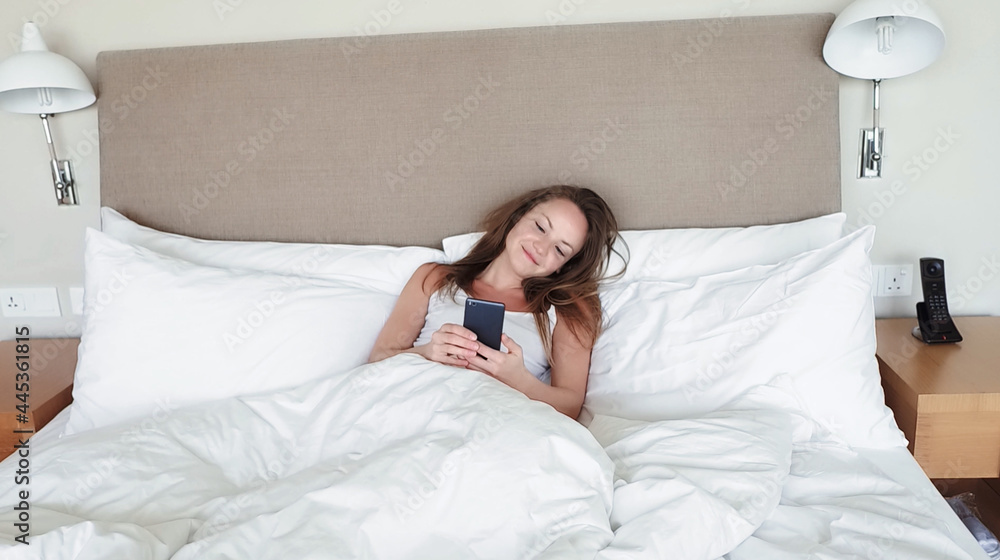Woman Lying In Bed Checking Messages On Mobile Phone Woman Lying In Bed Checking Messages On Mobile Phone