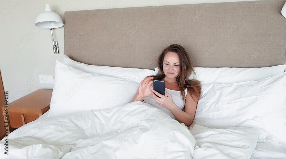 Woman Lying In Bed Checking Messages On Mobile Phone Woman Lying In Bed Checking Messages On Mobile Phone