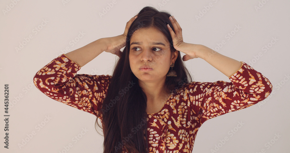 Young Indian woman with long brown hair holding her head while sighing ...