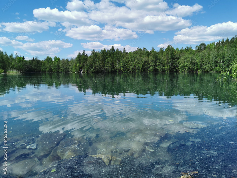 Fototapeta premium The shore of the lake is bright with clear water, in which you can see the marble on the bottom and reflect the sky with clouds, in the mountain park Ruskeala.
