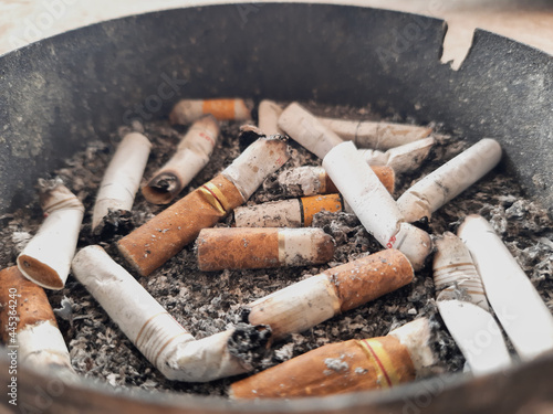 Cigarette butts in an iron ashtray placed on a concrete floor