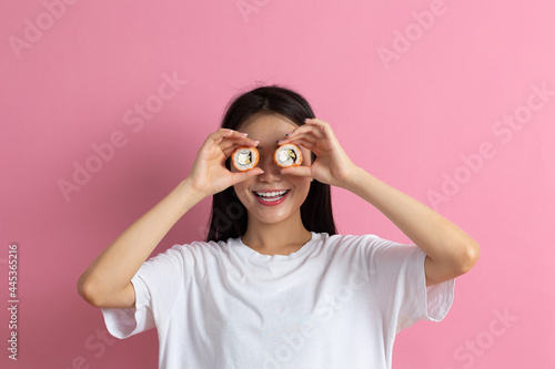 Asian beauty model girl eating Sushi roll  healthy japanese food. Beautiful woman holding Philadelfia roll near her eyes in hands like binoculars and looking for tasty sushi