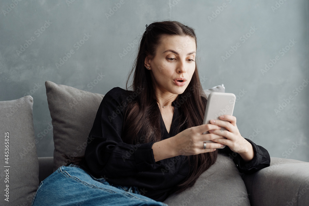 Surprised woman using smartphone while sitting on sofa Surprised woman using smartphone while sitting on sofa