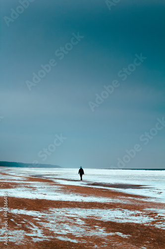 A single person walks alone on a snow-covered beach along the coast on a frosty cold day - A feeling of loneliness and solitude