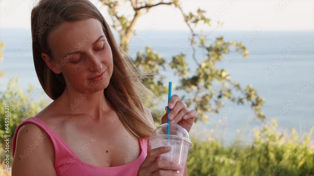 Vegan woman in pink dress is relaxing near sea cost with berry smoothie Vegan woman in pink dress is relaxing near sea cost with berry smoothie