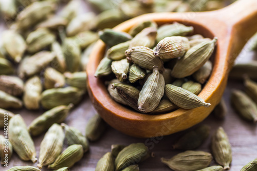 Green cardamom in a wooden scoop, aromatic spice used in the kitchen, providing many health benefits.

