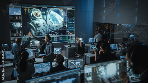 Fotografia Group of People in Mission Control Center Establish Successful Video Connection on a Big Screen with an Astronaut on Board of a Space Station