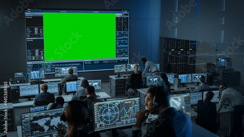 Big Green Screen Horizontal Mock Up in a Mission Control Center Room with Flight Director and Other Controllers Working on Computers. Team of Engineers Work in Monitoring Room Full of Displays.
