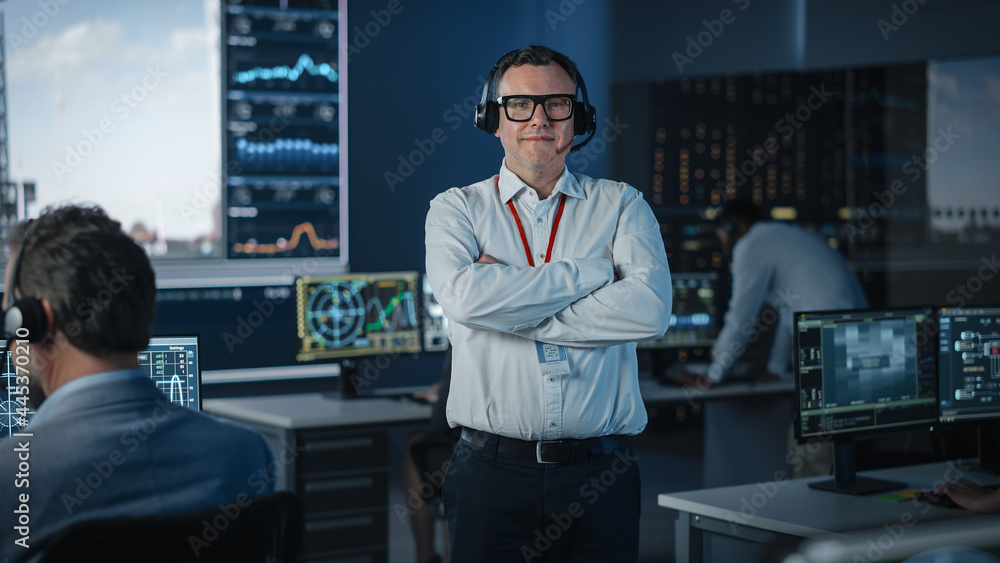 Fototapeta premium Portrait of a Happy Male Flight Controller Posing for Camera in a Mission Control Center. Successful Man Wearing a Headset and a White Shirt. Computer Screens in the Background.
