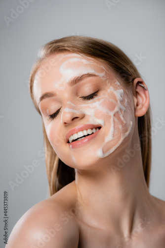 joyful woman with closed eyes and and cleansing foam on face isolated on grey