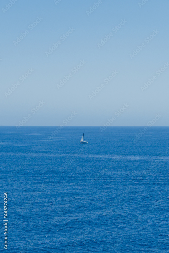 Mar azul en verano con un barco velero en medio de la imagen.