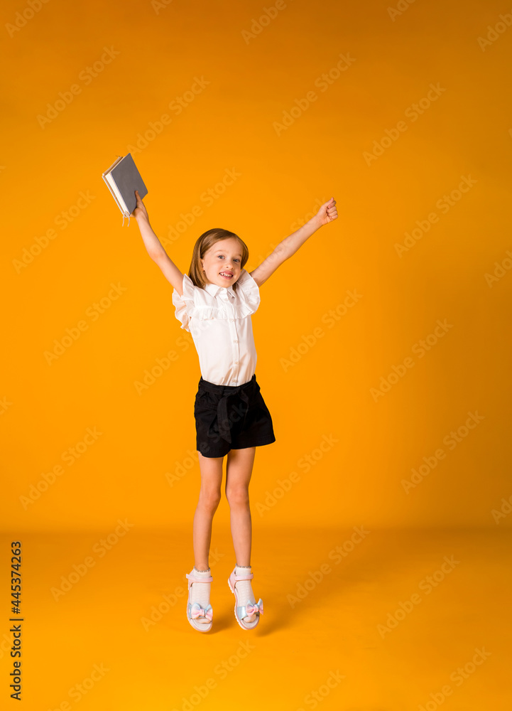 happy schoolgirl in a uniform jumps with a blue notebook on a yellow background with a copy of the space. Back to school happy schoolgirl in a uniform jumps with a blue notebook on a yellow background with a copy of the space. Back to school