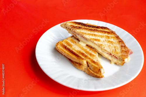 Toasted ham and cheese sandwich in white plate on red table cloth, The tosti in Netherlands or croque-monsieur is a hot sandwich made with ham and cheese. 