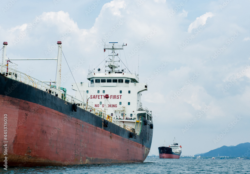Fototapeta premium Big logistic ship unloading in the ocean with view mountain on island background and cloudy on sky,Shipping boat economy transportation concept on the sea