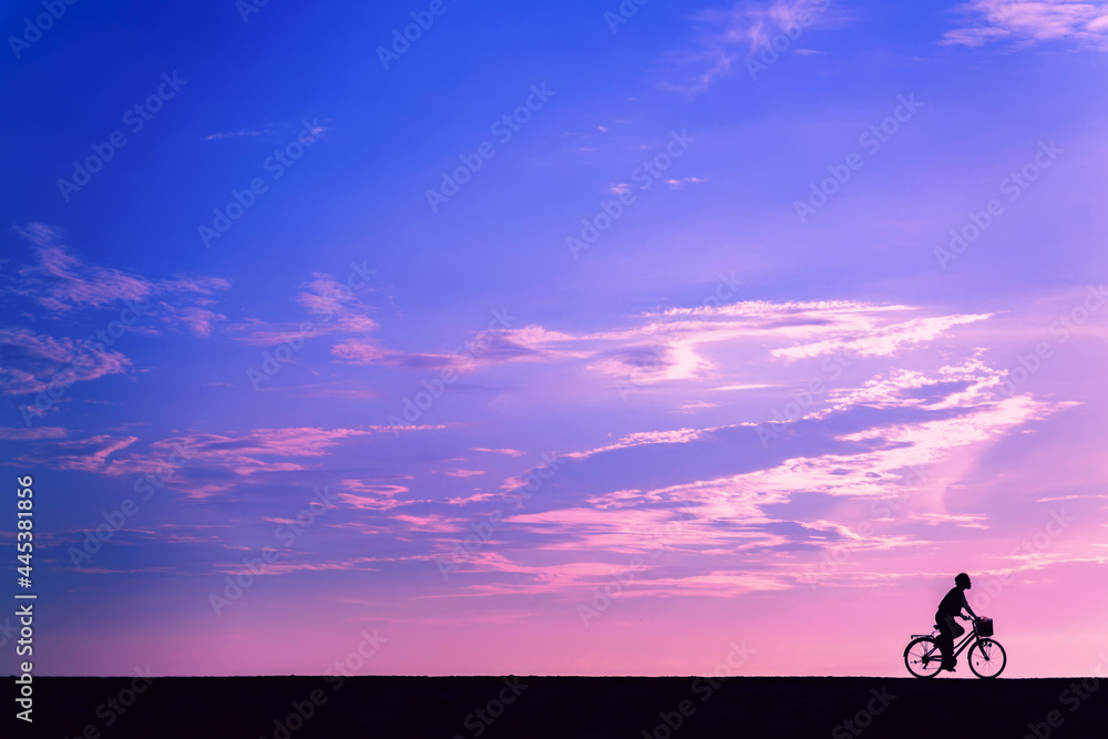 The silhouette of a cyclist at dawn. A man rides a bicycle with a basket on the background of a purple sky. Cyclist in Bali