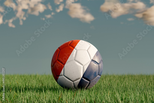 Soccer ball with the national colors of Netherland on a green meadow. Leather in slightly used look. Background blue with clouds. 3D illustration.