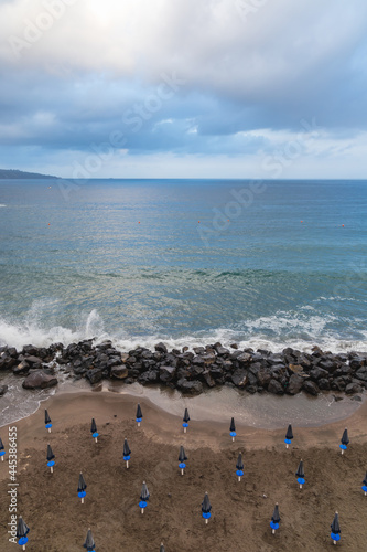 Fototapeta Naklejka Na Ścianę i Meble -  Big sea waves crash against the rocks next to beach full of umbrellas