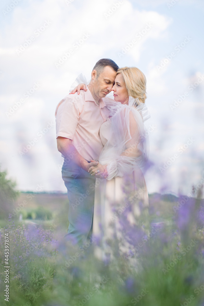 View through the lavender flowers. Happy middle aged couple, man and woman in elegant outfits, embracing and enjoying romantic moments together in the lavender field View through the lavender flowers. Happy middle aged couple, man and woman in elegant outfits, embracing and enjoying romantic moments together in the lavender field