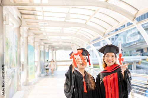 Two Asian women wore graduate gowns are throwing certificates and smiling widely.