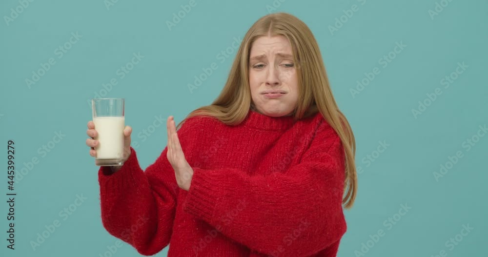 Concerned young woman with long blond hair dressed in a red sweater refuses to drink milk Concerned young woman with long blond hair dressed in a red sweater refuses to drink milk