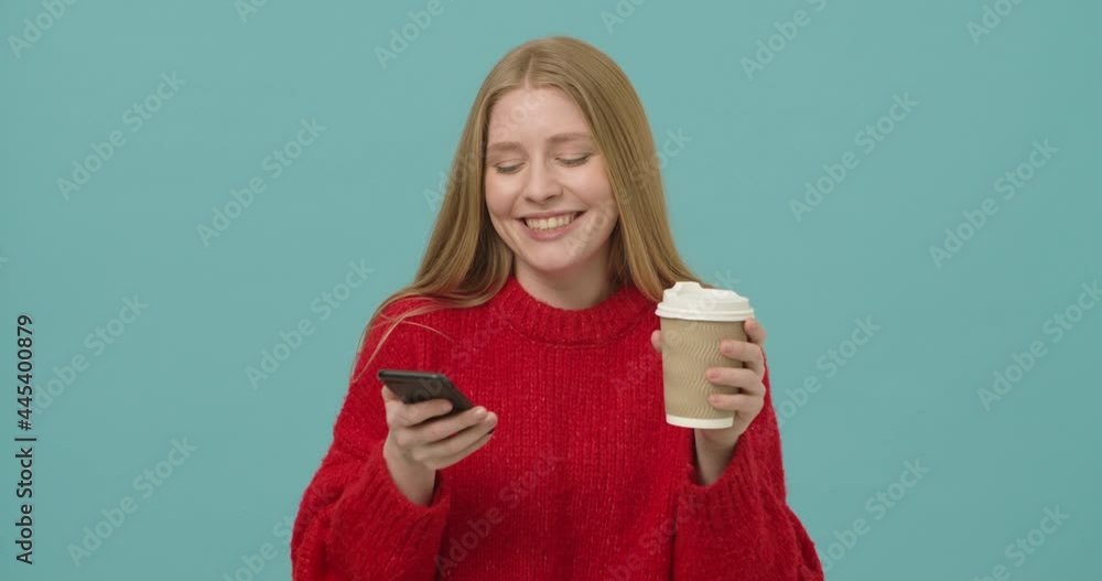 Young woman smiling looking at the screen of a smartphone holding cup of coffee to go Young woman smiling looking at the screen of a smartphone holding cup of coffee to go