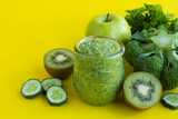 Green smoothie or puree in the small glass jar on the yellow background. Close-up.
