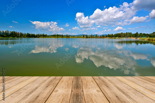 Empty wooden table and view of blurred calm lake with reflections white clouds background © Jurek Adamski
