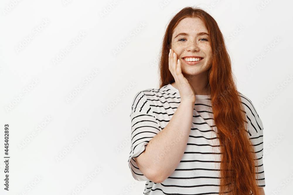 Beautiful redhead girl, young woman with red long natural hair and freckles, touching healthy clean and glowing skin, facial makeup, smiling white teeth, happy expression Beautiful redhead girl, young woman with red long natural hair and freckles, touching healthy clean and glowing skin, facial makeup, smiling white teeth, happy expression