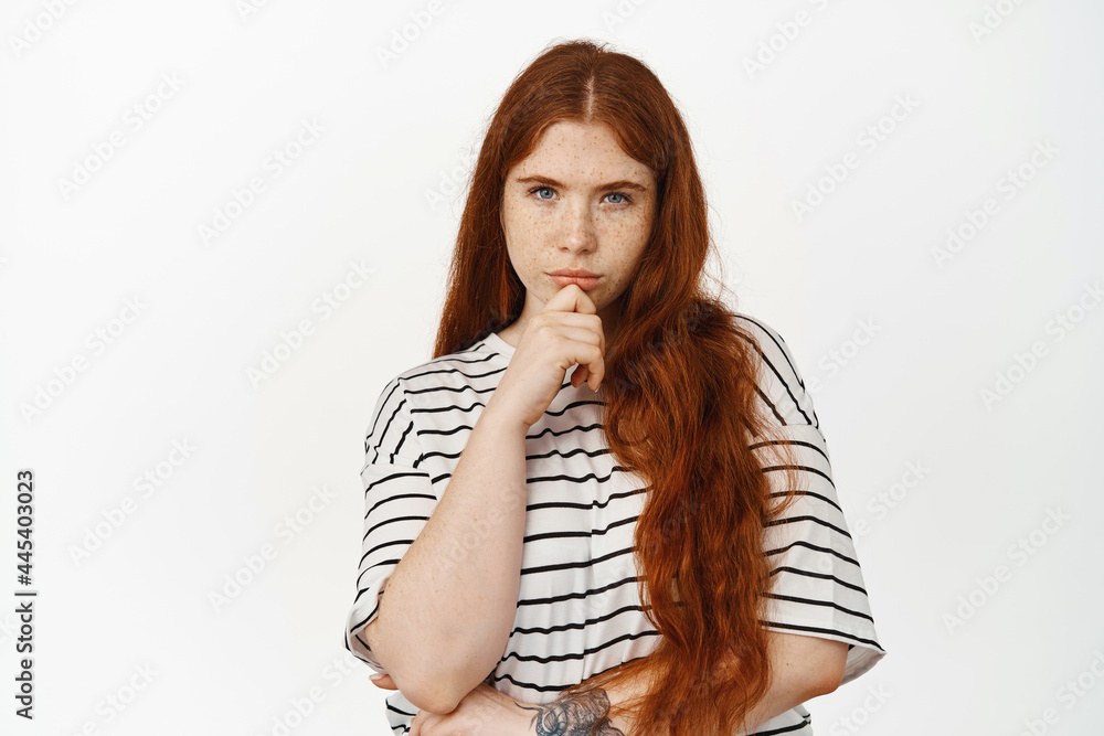 Image of thoughtful redhead teen girl squinting, touching chin, consider smth, thinking, making decision, ponder choices, standing against white background Image of thoughtful redhead teen girl squinting, touching chin, consider smth, thinking, making decision, ponder choices, standing against white background
