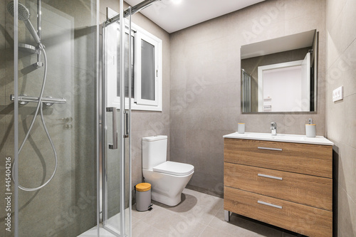 Modern refurbished bathroom with shower zone  toilet  wooden base with white sink and mirror.
