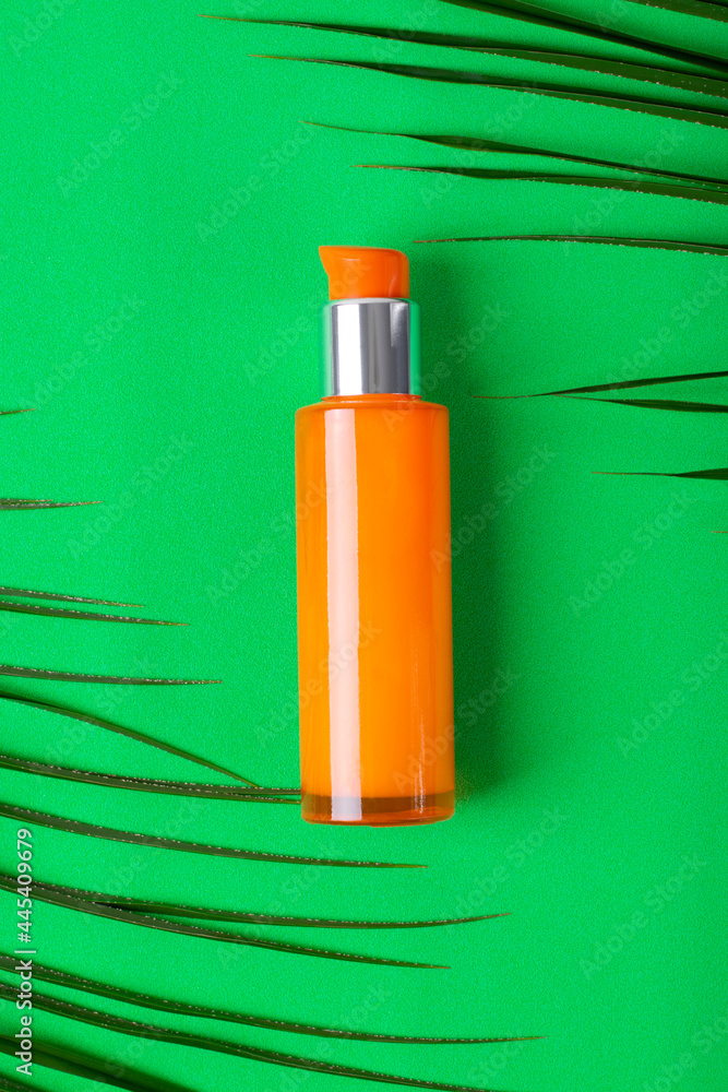 Orange dispenser bottle on green background with palm leaves. Organic skincare product. Unlabeled container Orange dispenser bottle on green background with palm leaves. Organic skincare product. Unlabeled container