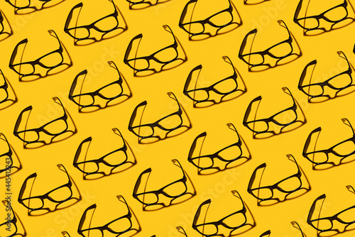 Pattern of rows of simple classic eyeglasses flat laid against yellow background photo