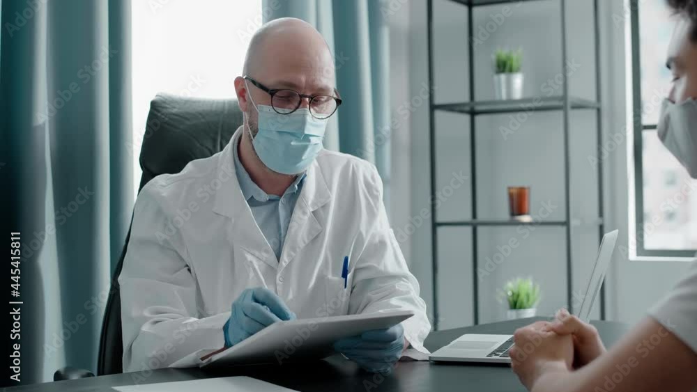 Professional bald doctor in blue face mask examines patient Professional bald doctor in blue face mask examines patient