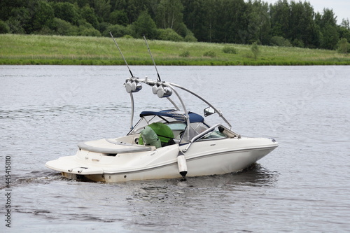 White motor boat with targa on river water on green grassy forest shore background at summer day, back side view, active outdoor recreation watersports in Russia © Ilya