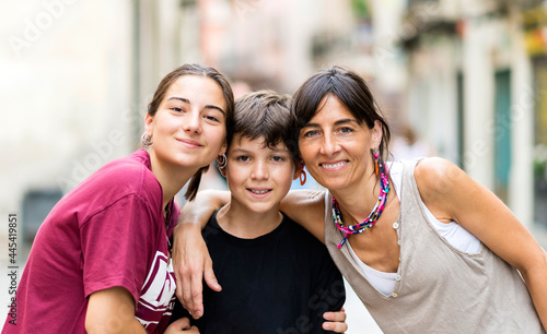 Portrait of three nice lovely cheerful affectionate people mom teen daughter and little son embracing outside sunny day